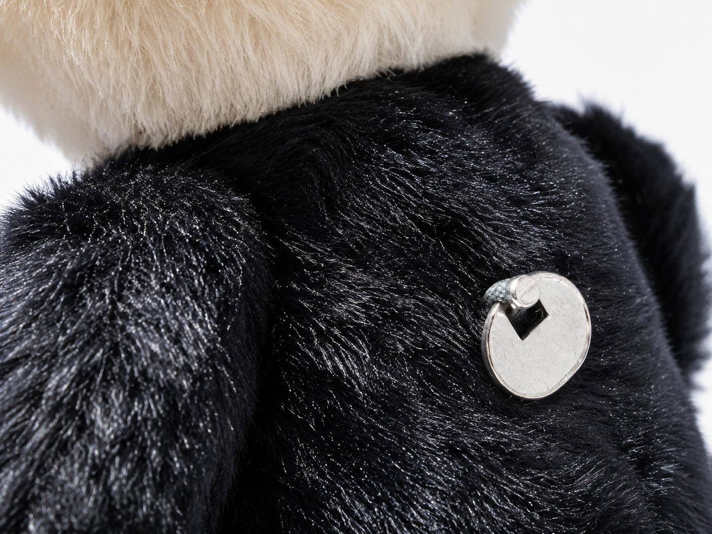 Makro Detailaufnahme der silbernen Metallplakette auf dem schwarzen Stoff des Steiff Dr. No Teddybären
