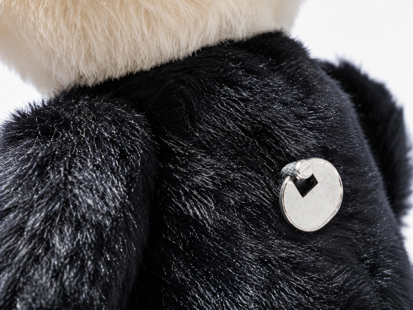 Makro Detailaufnahme der silbernen Metallplakette auf dem schwarzen Stoff des Steiff Dr. No Teddybären